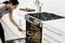A person places a pan with fried meat into the oven. The kitchen is modern and clean, with white cupboards and a marble worktop.