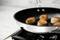 Six seared scallops in a pan on a hob. They are golden brown and clearly in the process of cooking.