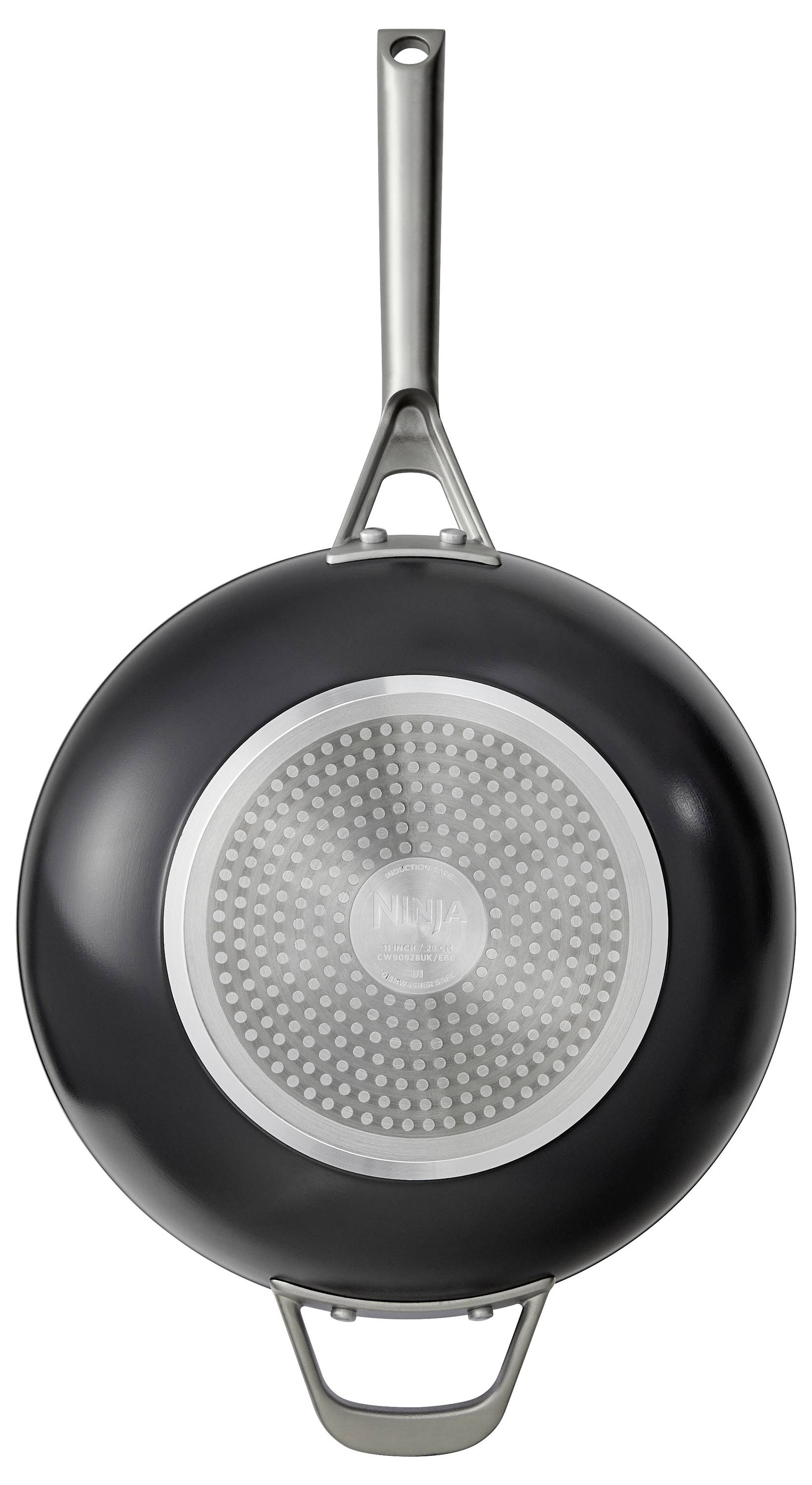 Black frying pan with a metal handle and silver reverse side, hanging on the wall, shows the design of the pan's underside.