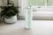 A mint green thermos flask sits on a kitchen worktop next to a plant in front of a window.