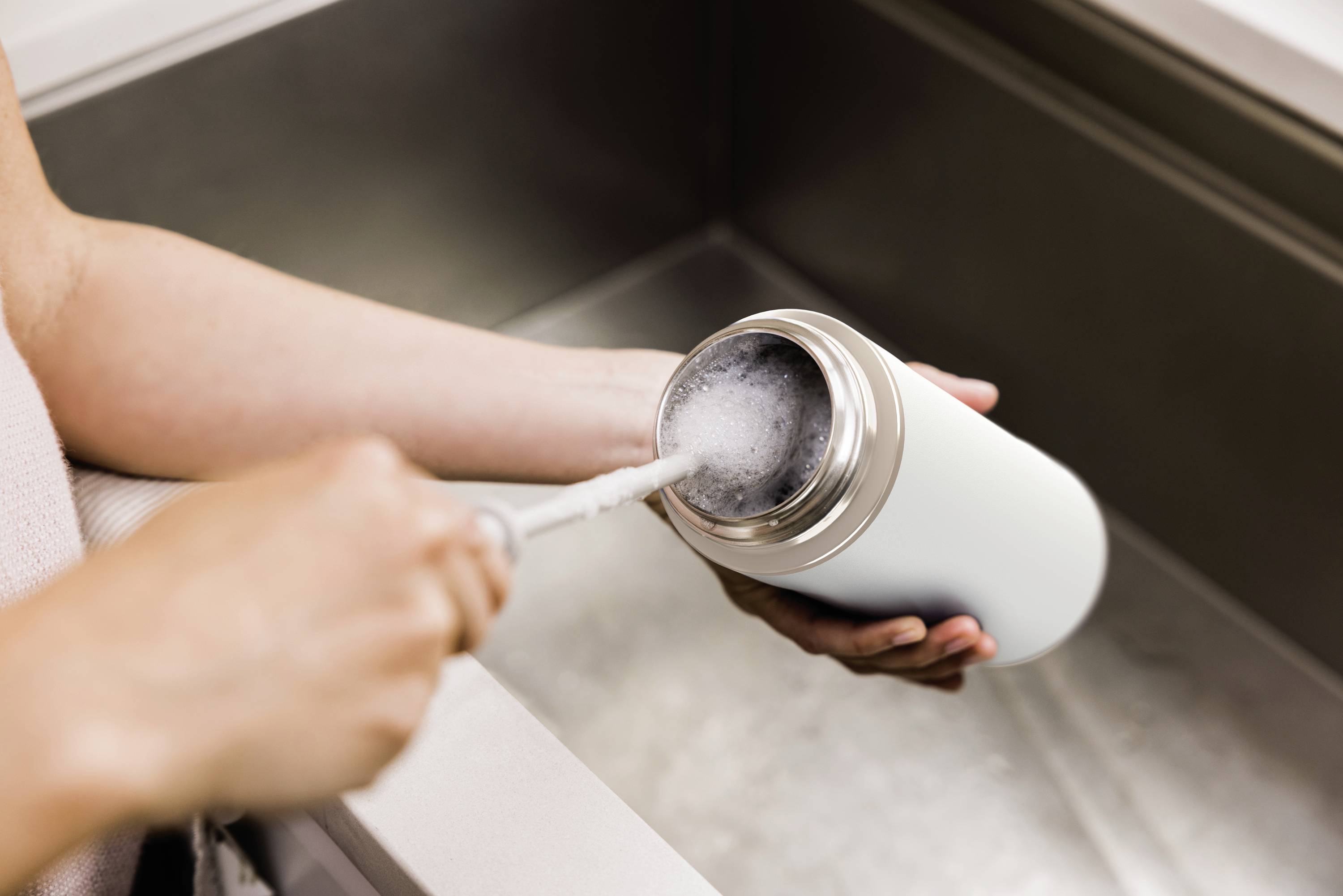 A person is cleaning a white water bottle with a brush over a sink.