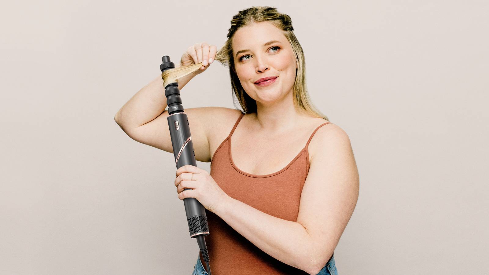 A woman demonstrates the use of an automatic curling tong on her hair. She is wearing a sleeveless top and smiling slightly.