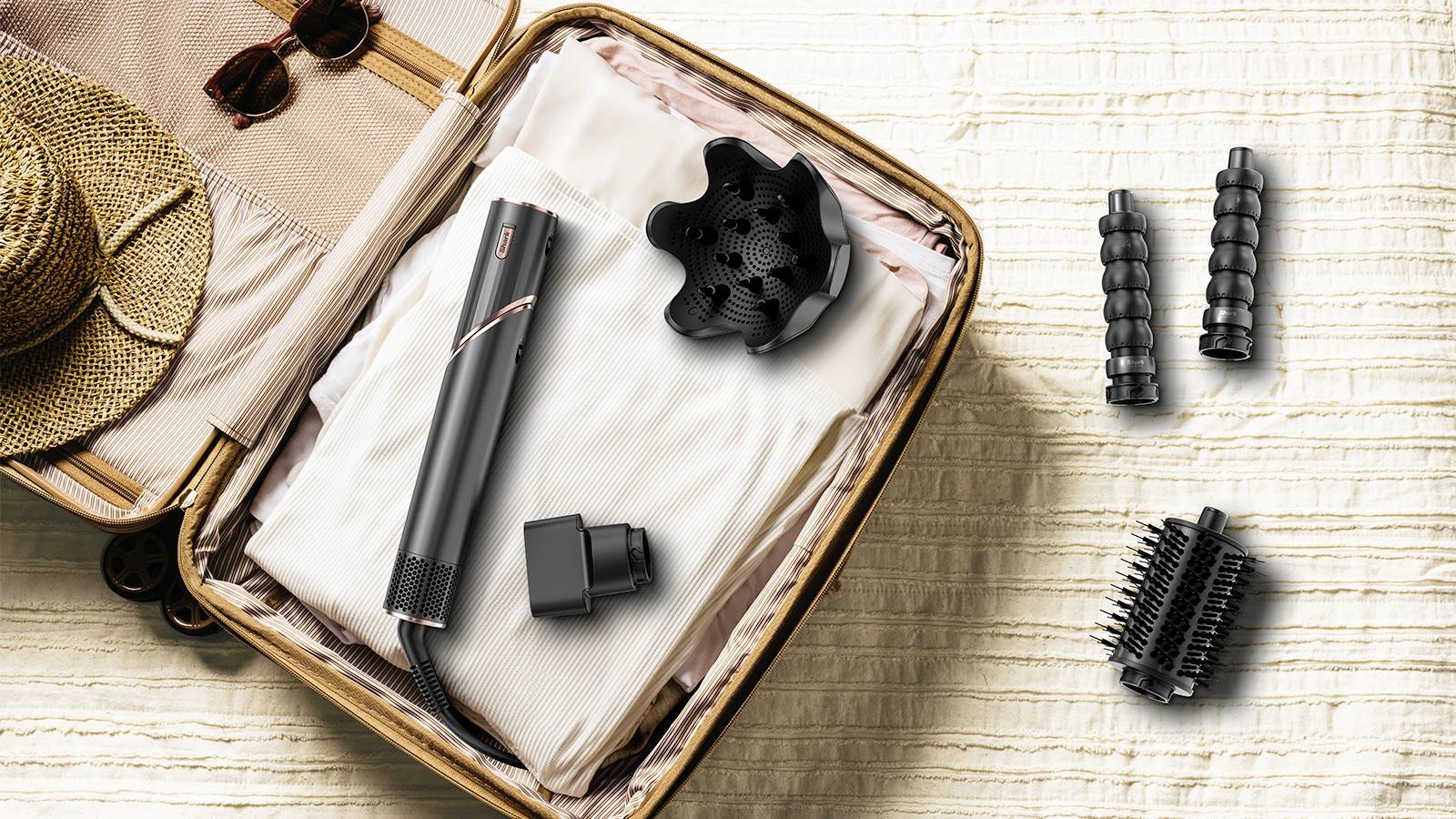 An open suitcase with a beige jumper, a straw hat, and a hairdryer with accessories such as attachments laid out beside the case.