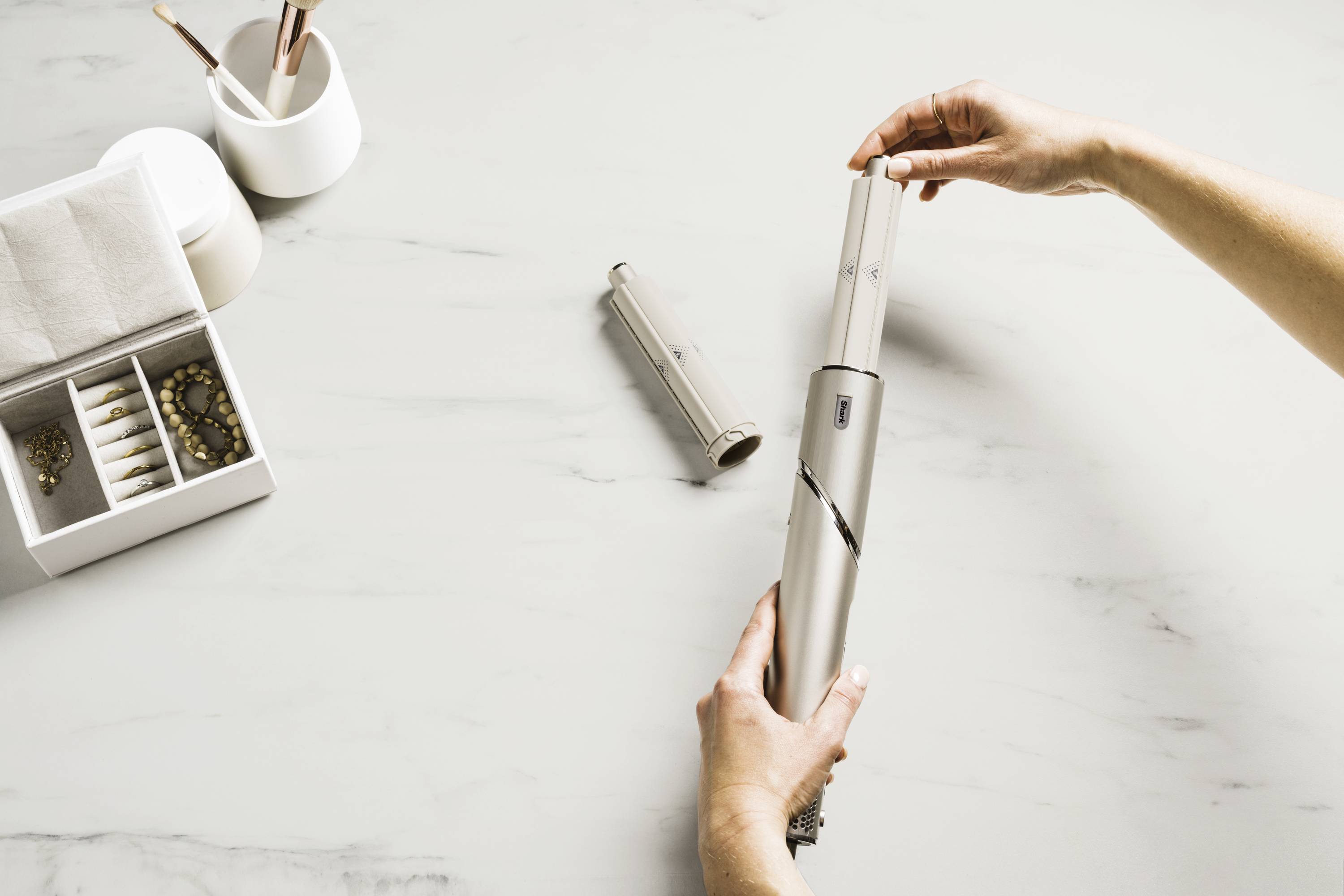 A person demonstrates the use of a vacuum cleaner storage system on a marble tabletop, with a jewellery box in the background.