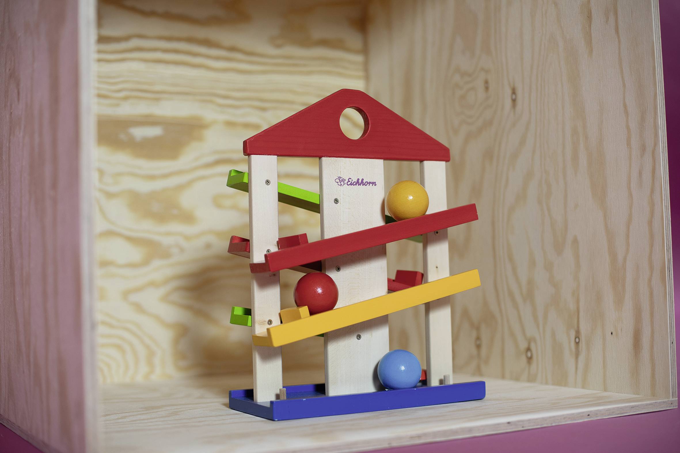 Wooden toy with a red roof and colourful tracks for marbles to roll along. Presented in a wooden box.