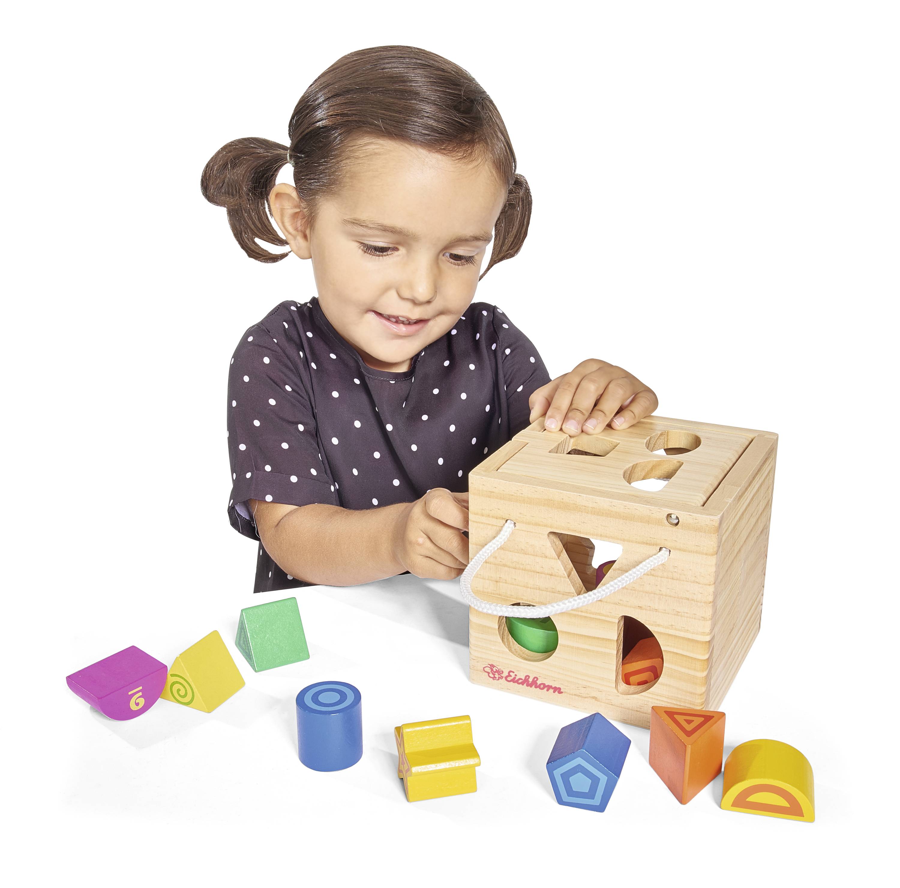 A child places colourful shapes into a wooden box. The toy helps develop motor skills and shape recognition.