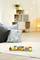 Wooden toy train on a light-coloured carpet in a cosy living room with cushions, shelving, and plants in the background.