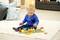 A small child sits on a carpet playing with a colourful wooden train. Living room in the background with a sofa and cushions.