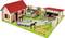 Toy farmyard with animals and figurines: horses, cows, pigs and geese on a green yard with a red roof.