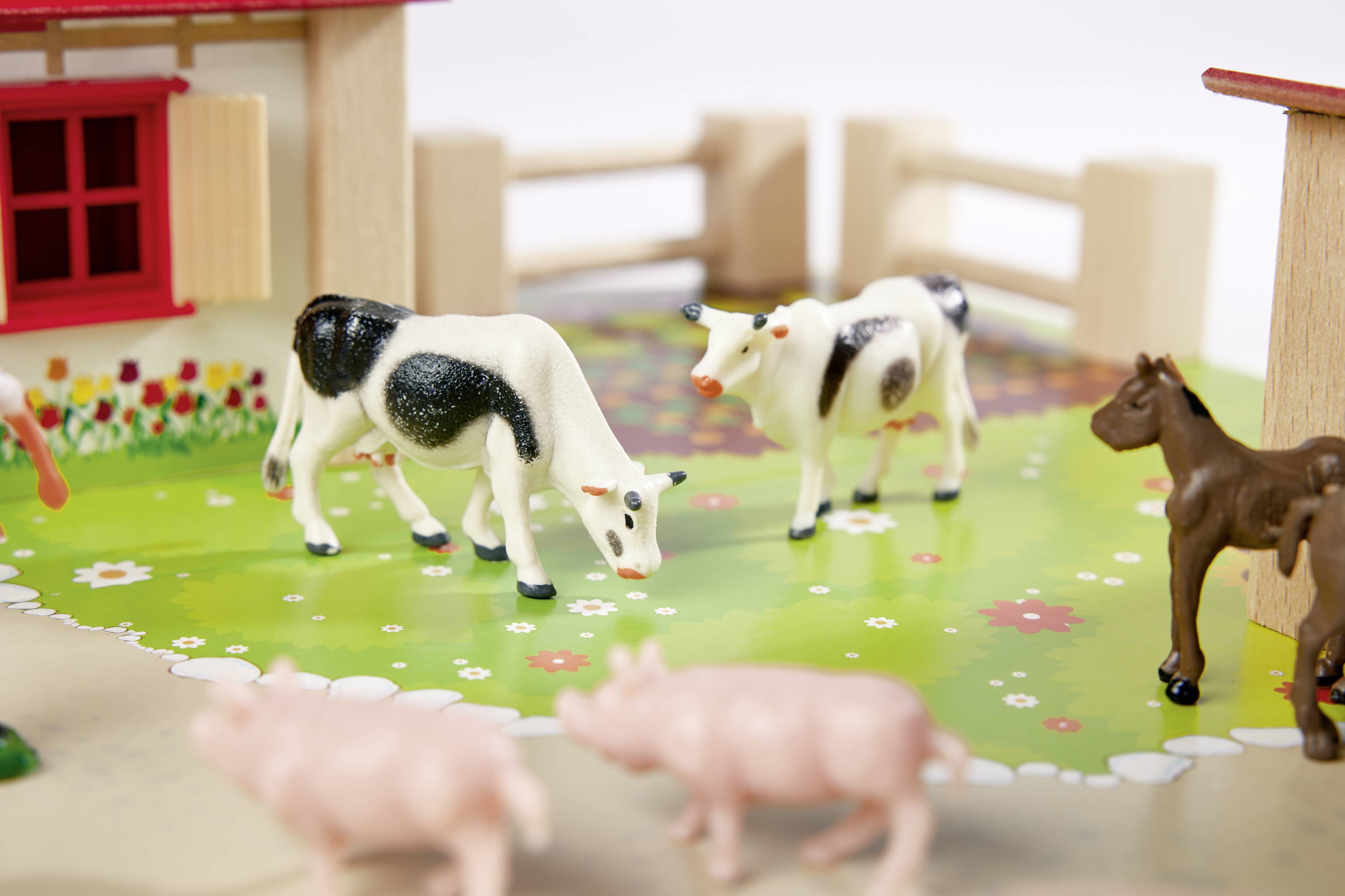 Plastic animals on a toy farm. Two cows grazing on a green surface, surrounded by pigs. A horse in the background.