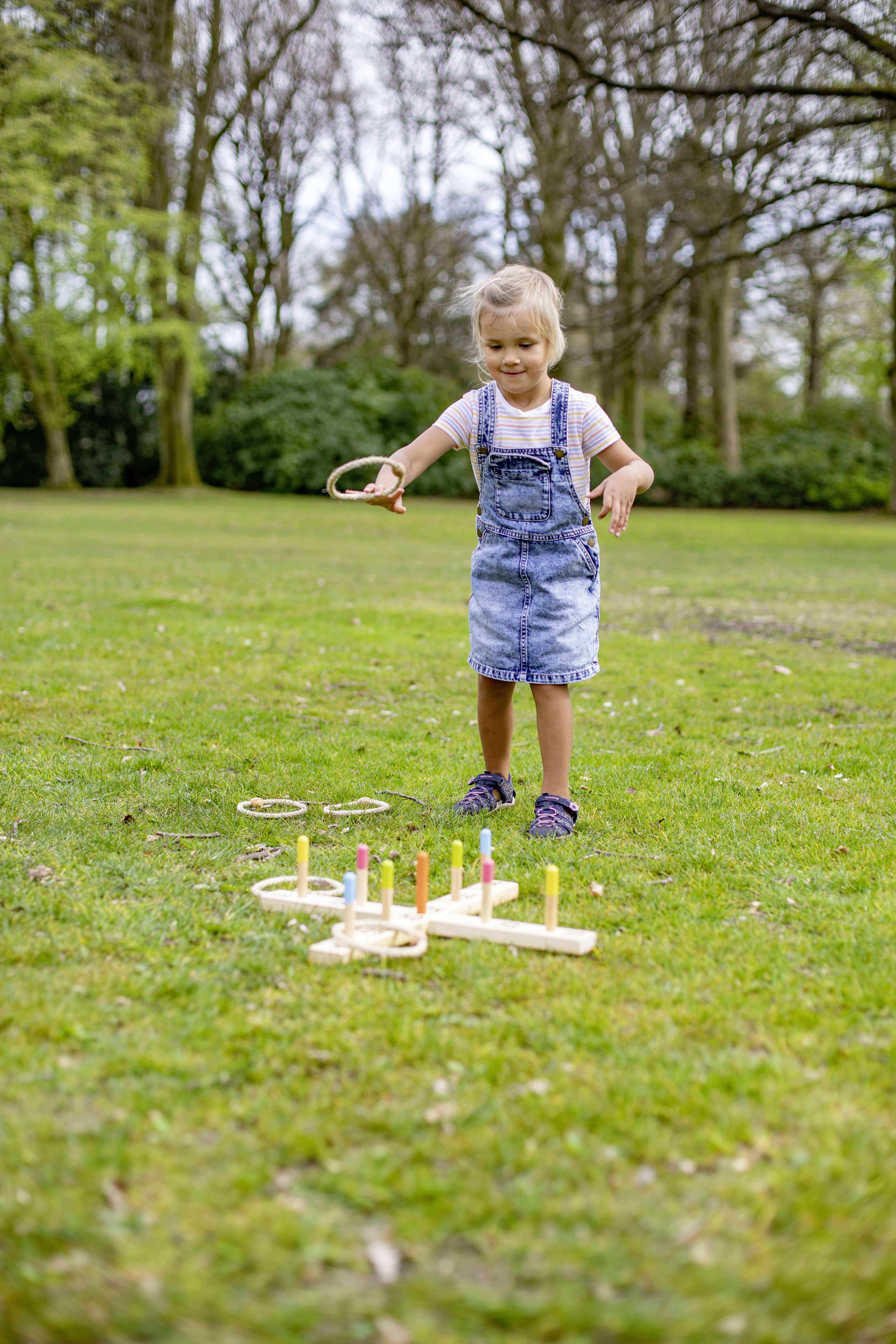 A child is playing a ring toss game outdoors on a meadow. They are throwing rings onto colourful wooden stakes to score points.