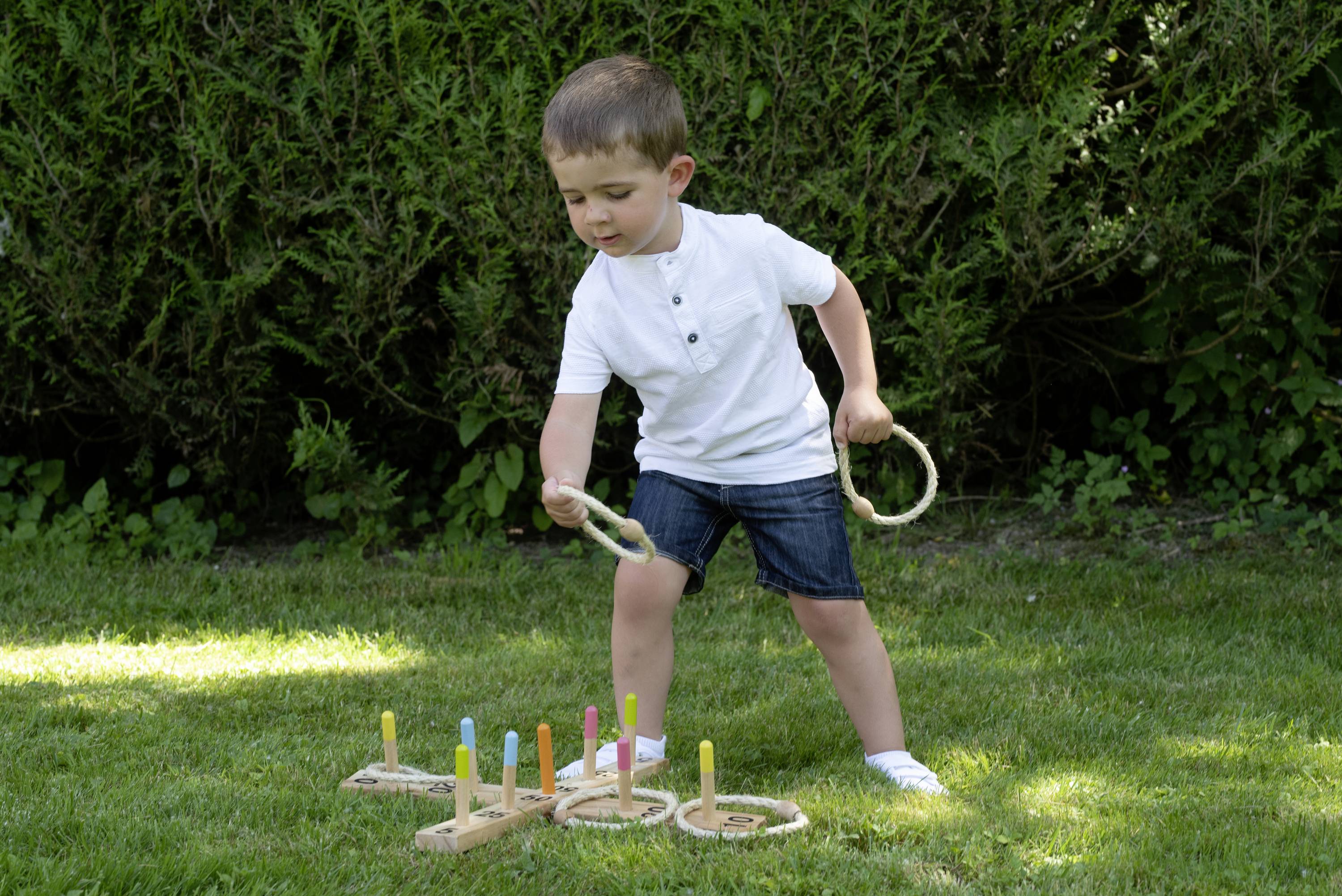 A child is playing a throwing game with rings in the garden. They are aiming at coloured sticks positioned on the lawn.