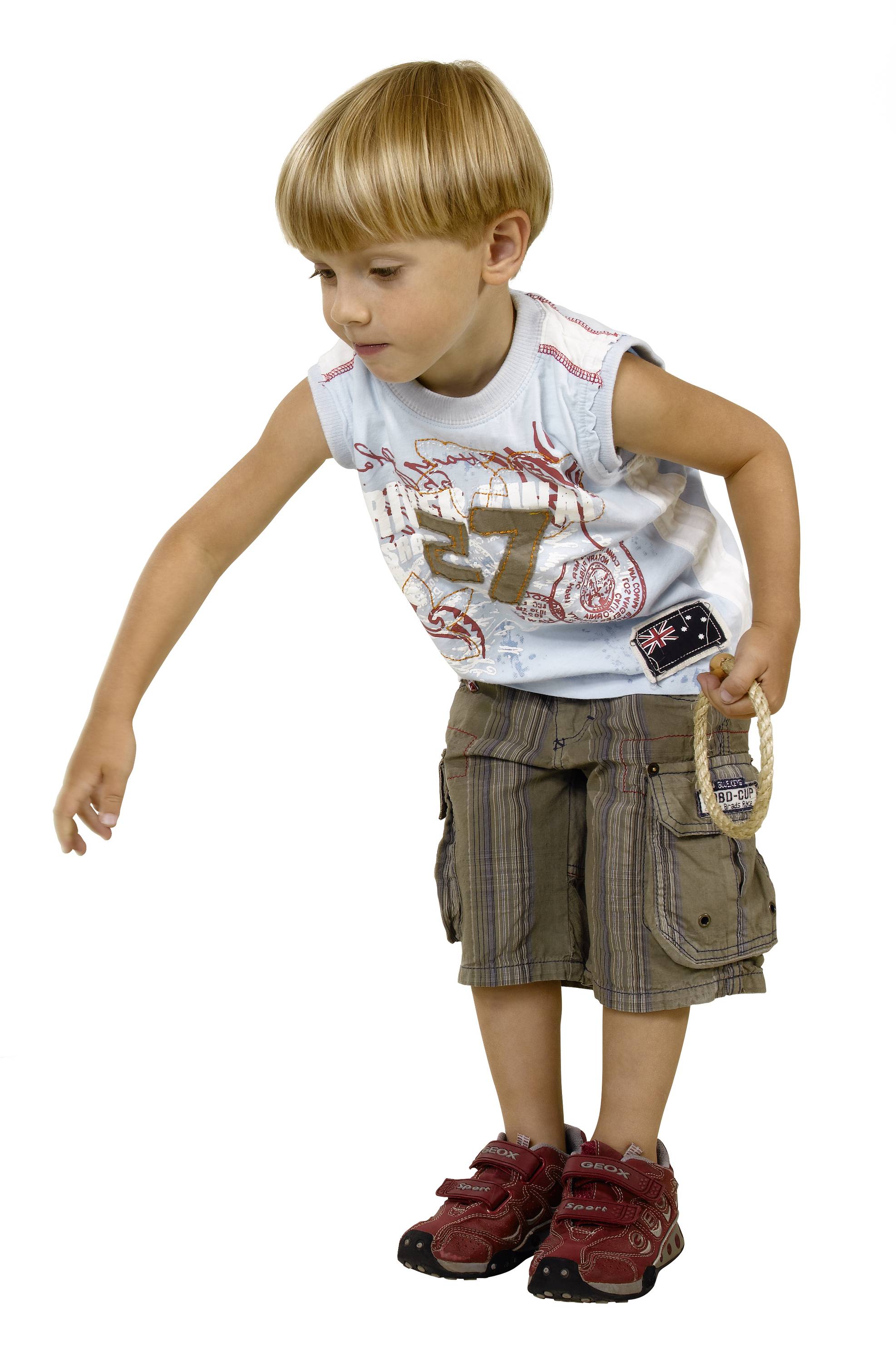 A boy in summer clothing is holding a hoop in his hand. He looks intently at the ground as if examining something.