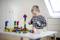 A small child is happily playing with colourful wooden building blocks at a table in a bright room.
