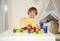 A small child is playing with colourful building blocks on a white table in front of a play tent in the background.