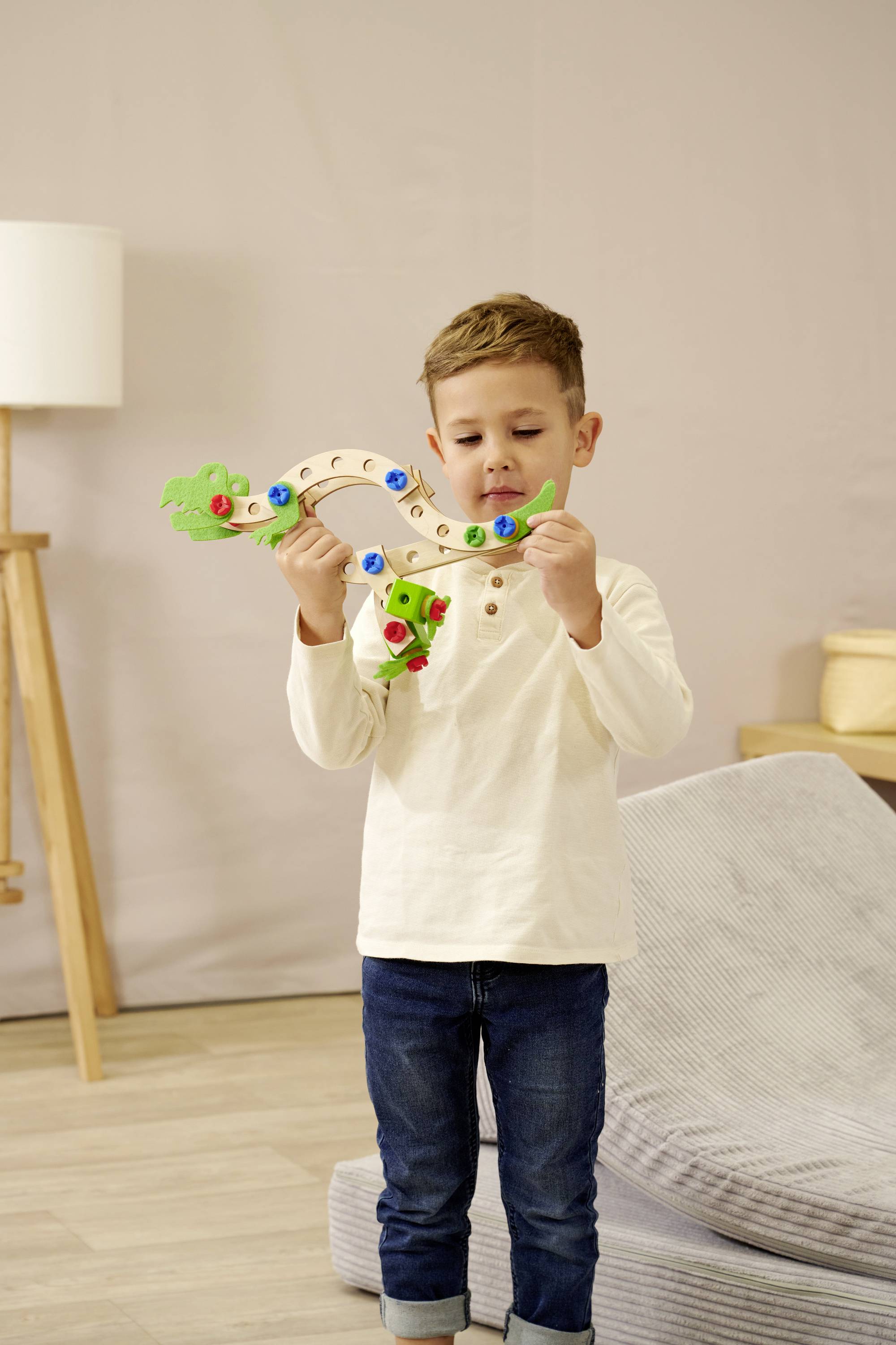 A child in casual clothing plays intently with a flexible, colourful toy kite in a cosy room.
