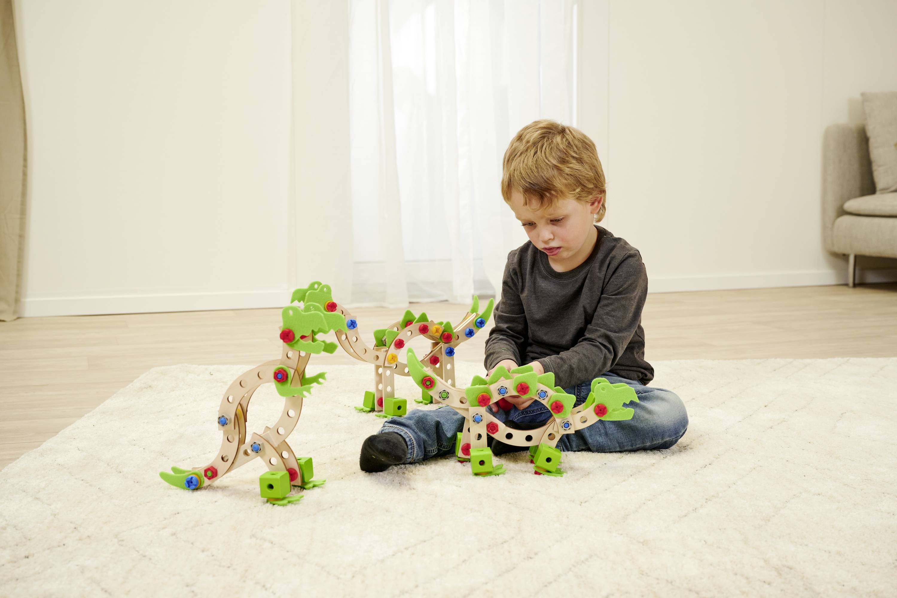 A child is playing on a carpet with wooden building blocks in dinosaur shapes in a living room.