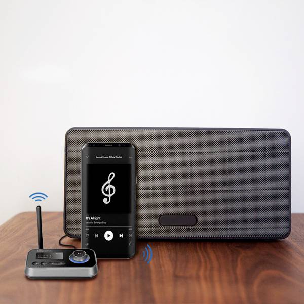 A smartphone is playing music and is connected to a speaker via a wireless device to transmit the sound.