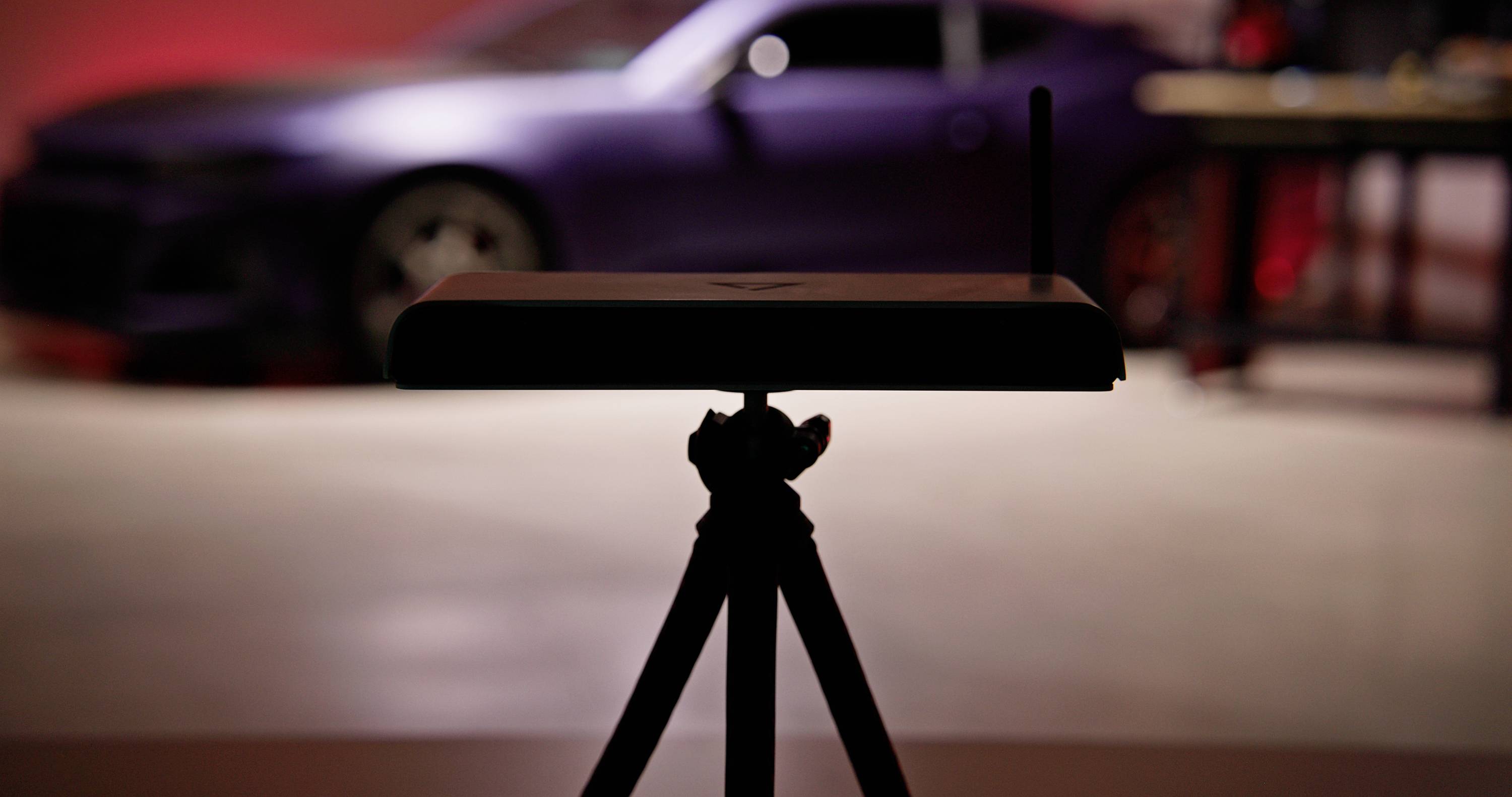 A router on a stand in the foreground with a blurred car in the background, slightly recognisable by its shape and colours.