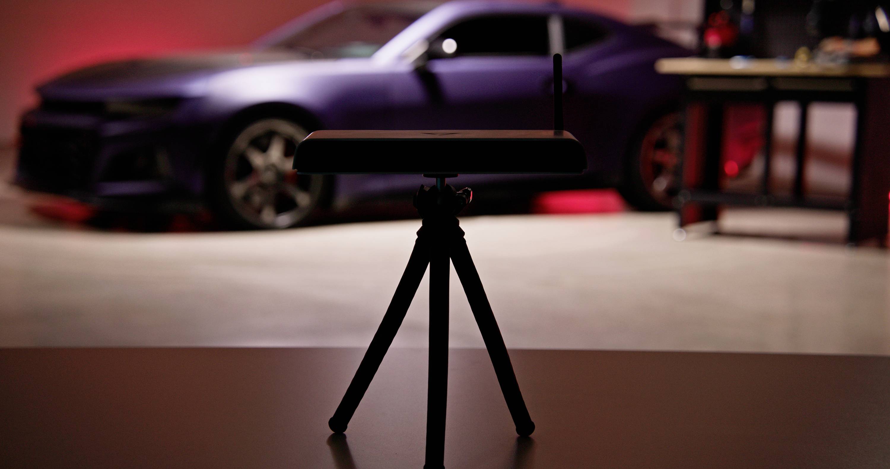 A router on a stand is in the foreground, with a blurred, sporty car in the background of a garage.