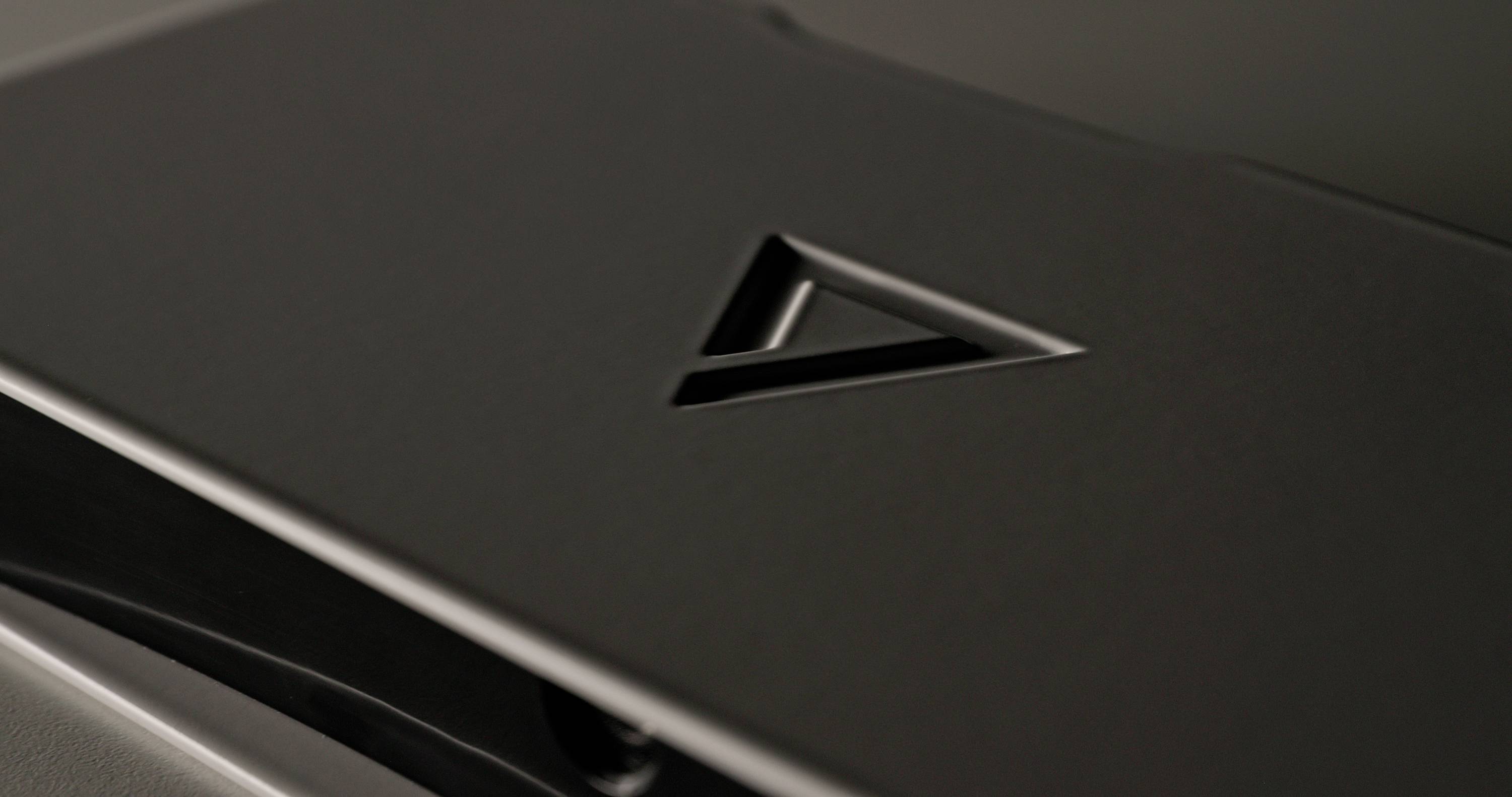 Black object with an embossed triangular symbol on its surface. The background is blurred, causing the symbol to stand out.