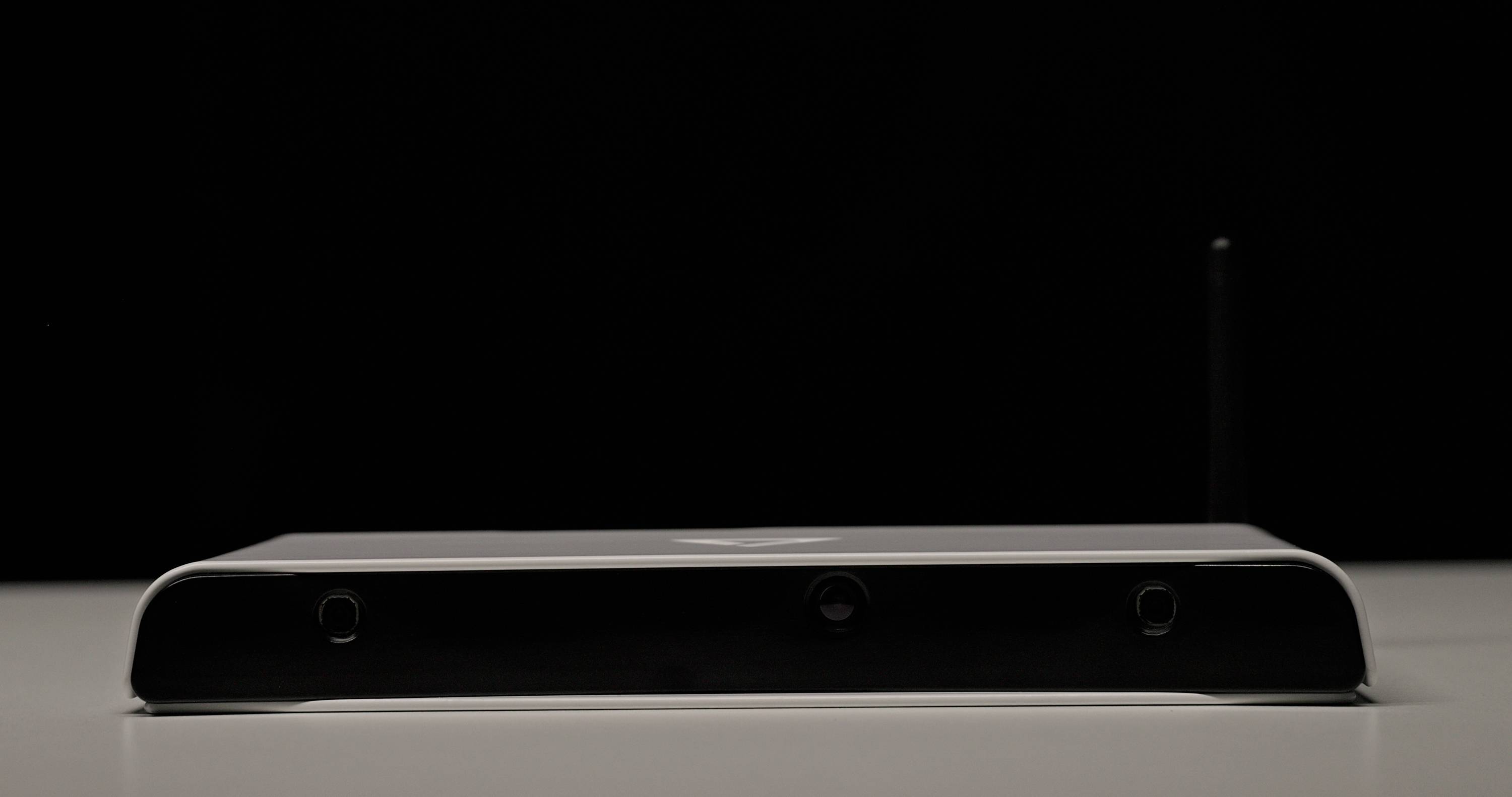 A black, flat electronic box with a small antenna, on a white surface against a black background.