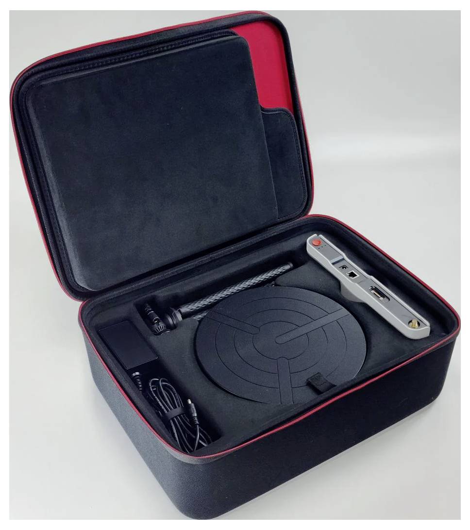 'Open black and red box with electronic devices: Circular platform, elongated metal arm, cables, adapters.'