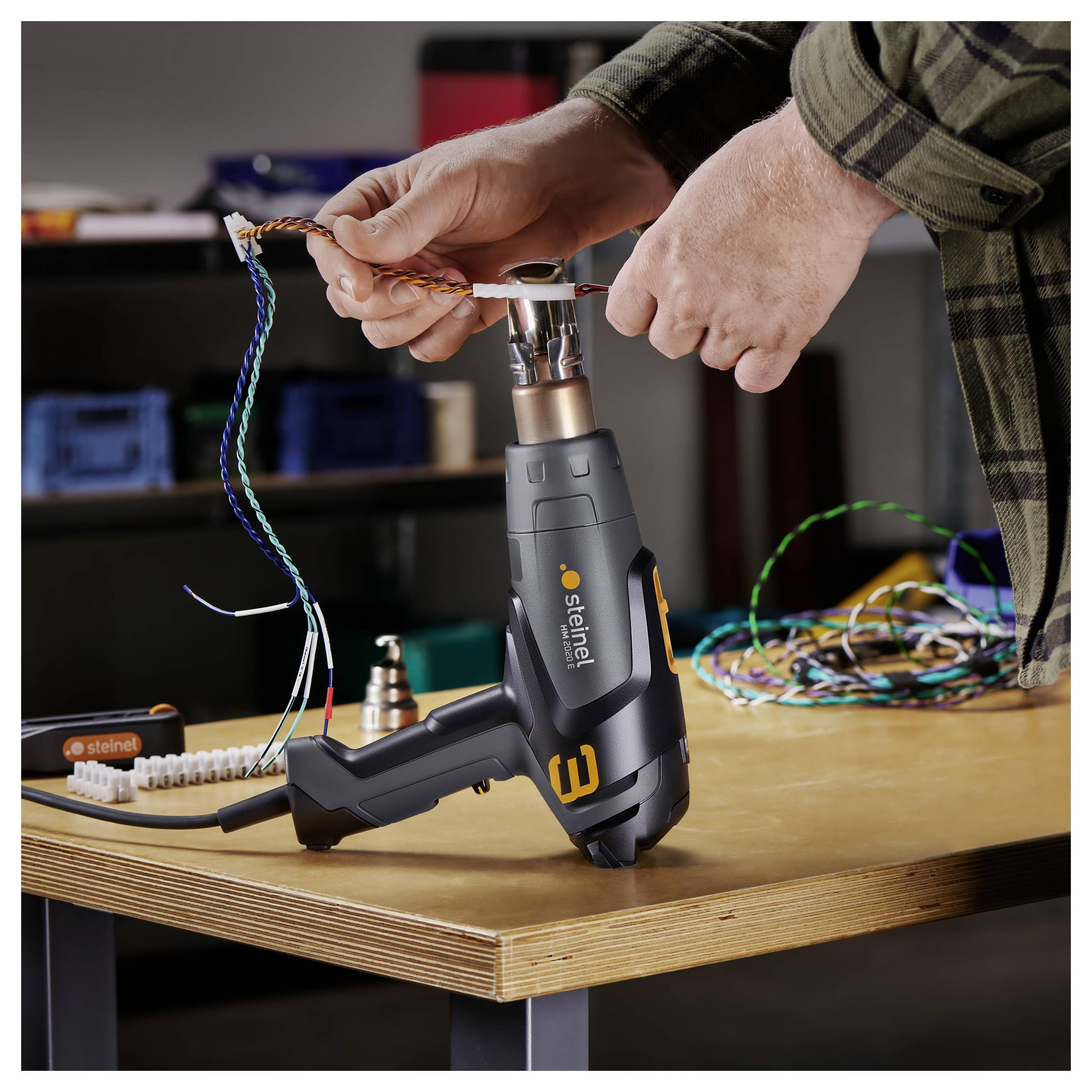 Person uses a heat gun to strip insulation from a twisted electrical wire on a workbench.