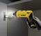 A gloved hand holds a yellow cordless drill, securing a hinge to a cabinet.