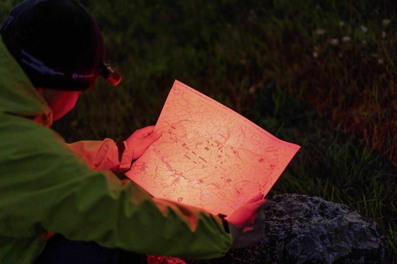A person wearing a head torch examines a map illuminated by red light at night.