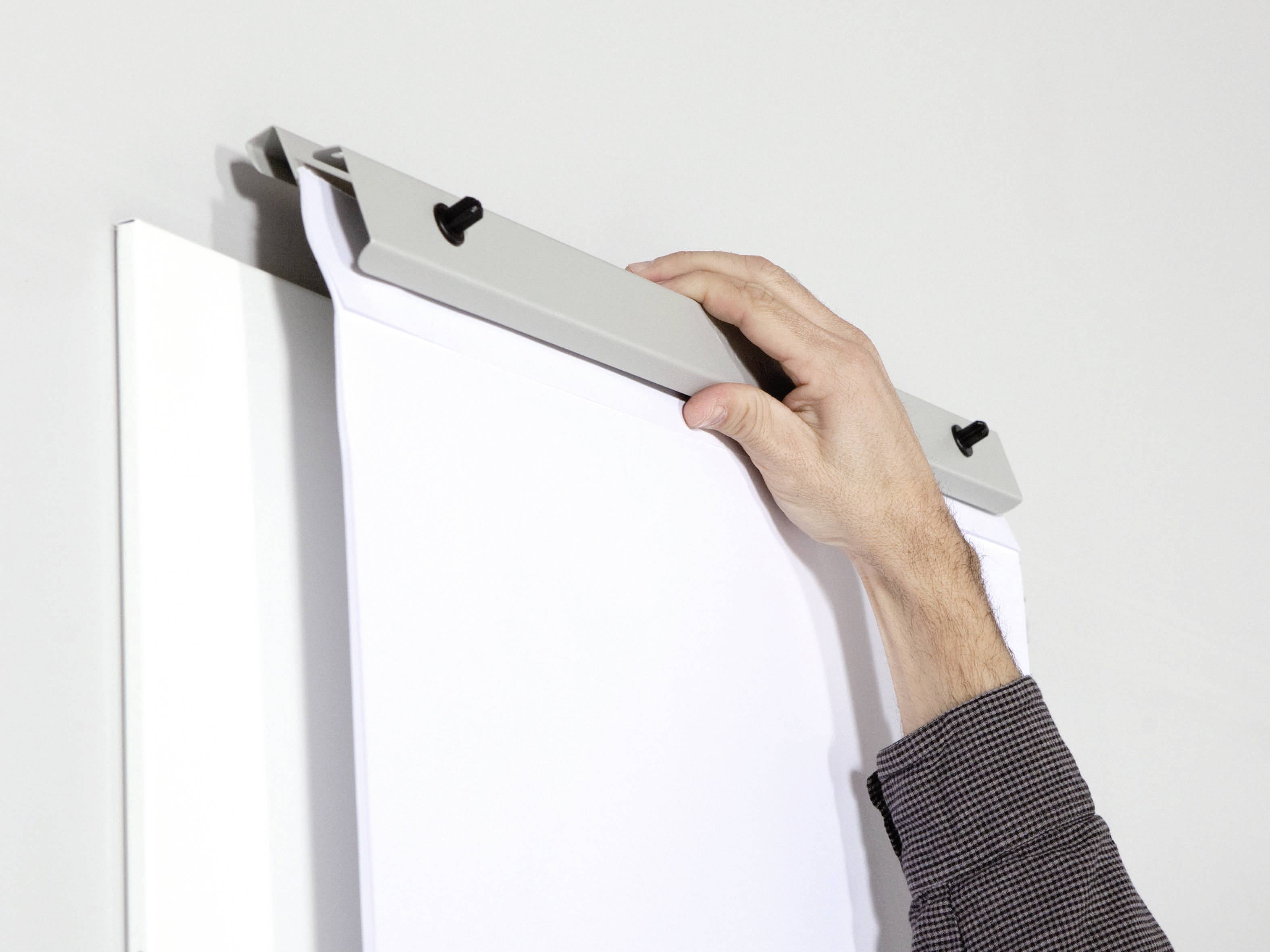 A hand hangs a sheet of paper on a clipboard.