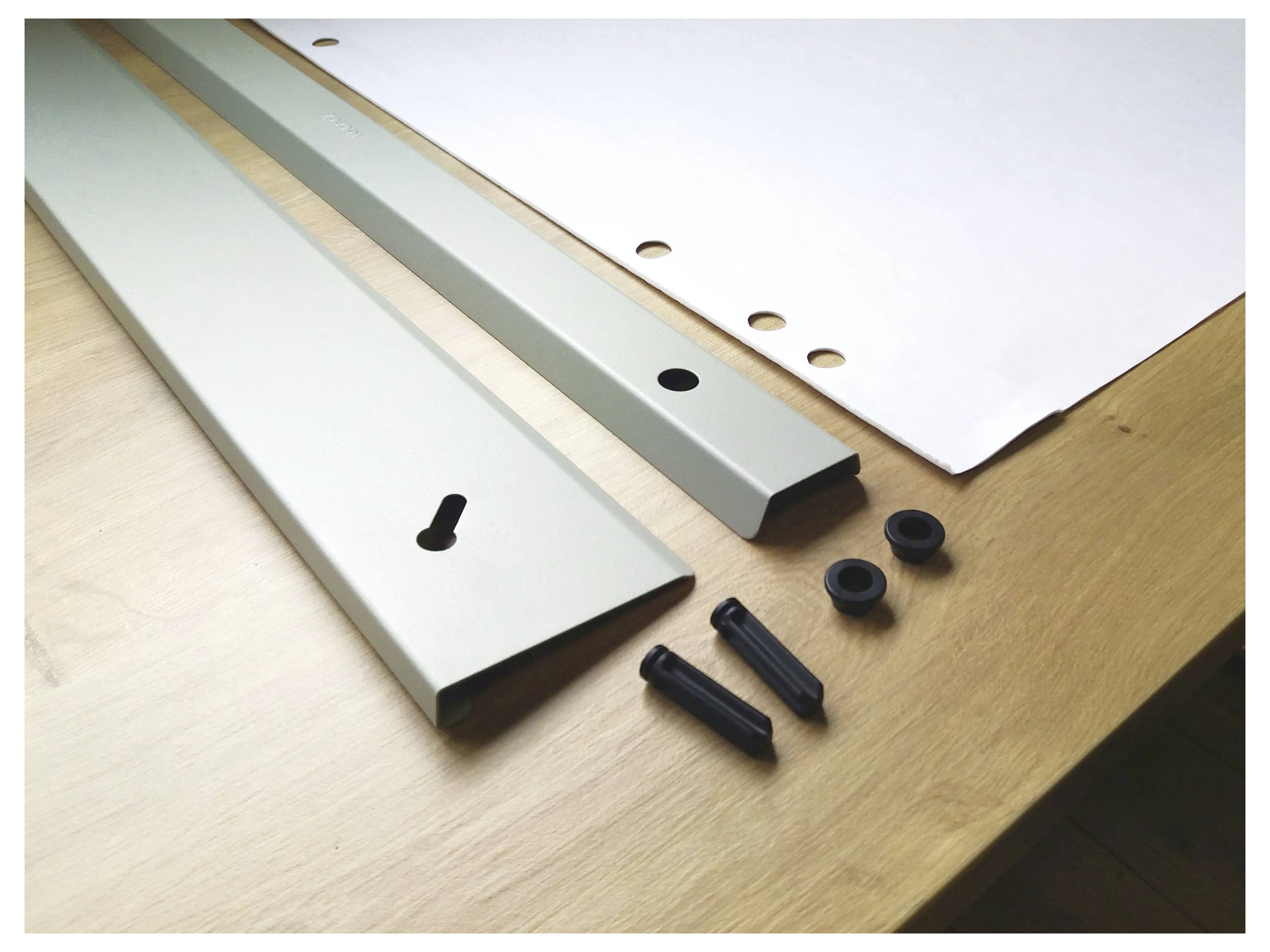 Metal strips and black screws, nuts, and washers are lying on a table next to a white sheet with holes.