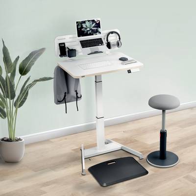 An adjustable-height desk with a laptop, headphones and desk accessories, surrounded by a plant and a stool.