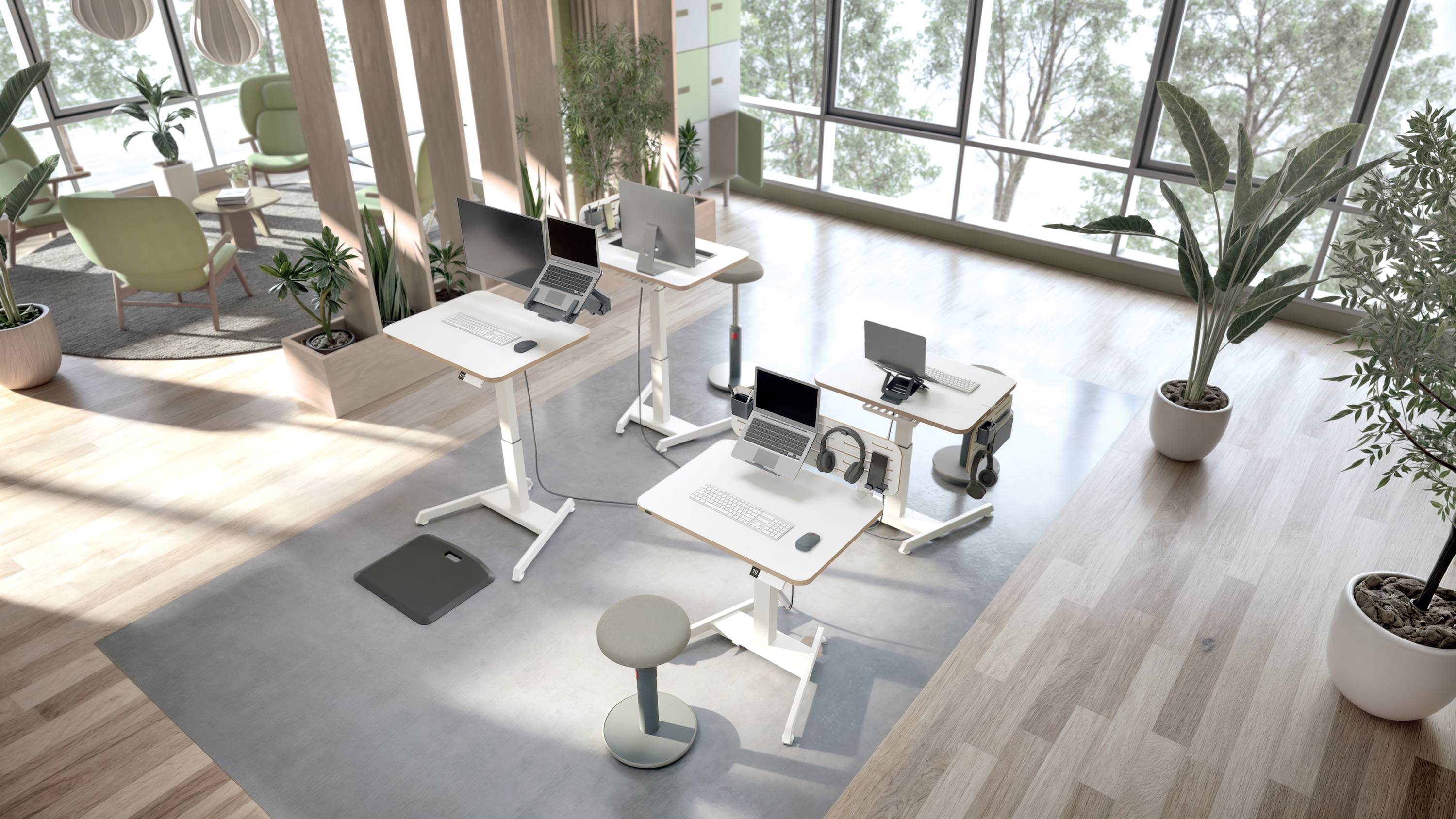 Modern office environment with height-adjustable desks and laptops, surrounded by large windows and plants that create a bright atmosphere.