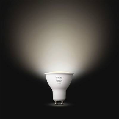 A Philips Hue light bulb radiates warm white light against a dark background.