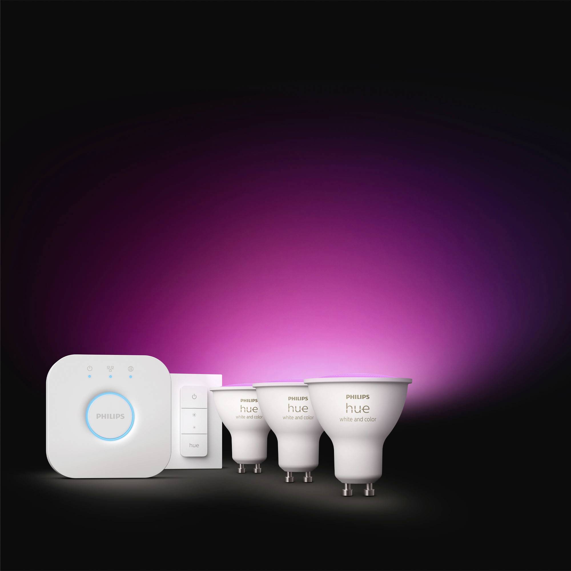 A Philips Hue lighting system with three smart light bulbs and a remote control, displaying a magenta-coloured illumination.