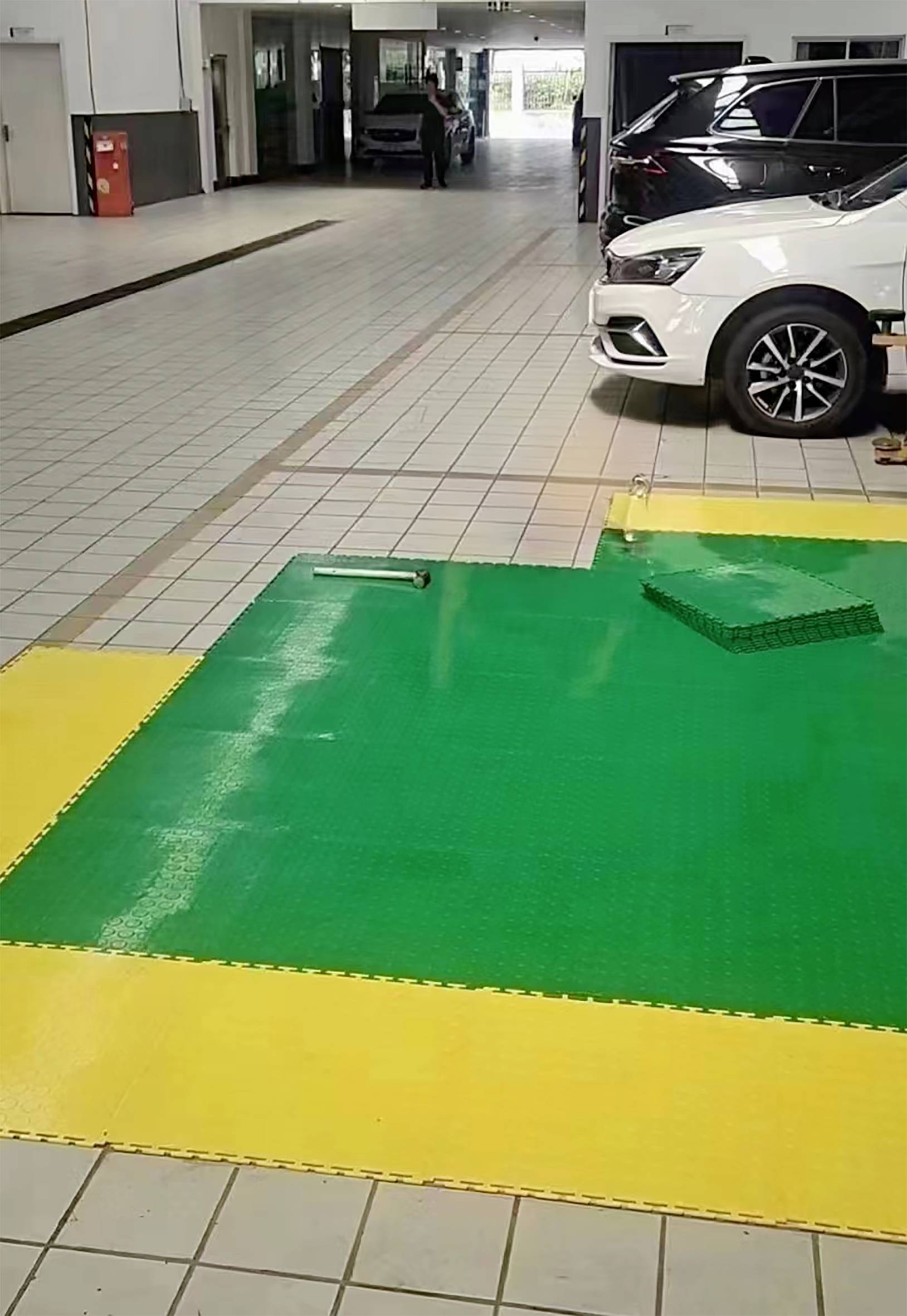 Green and yellow floor mats on a tiled floor in a car workshop, with a white car parked in the background.