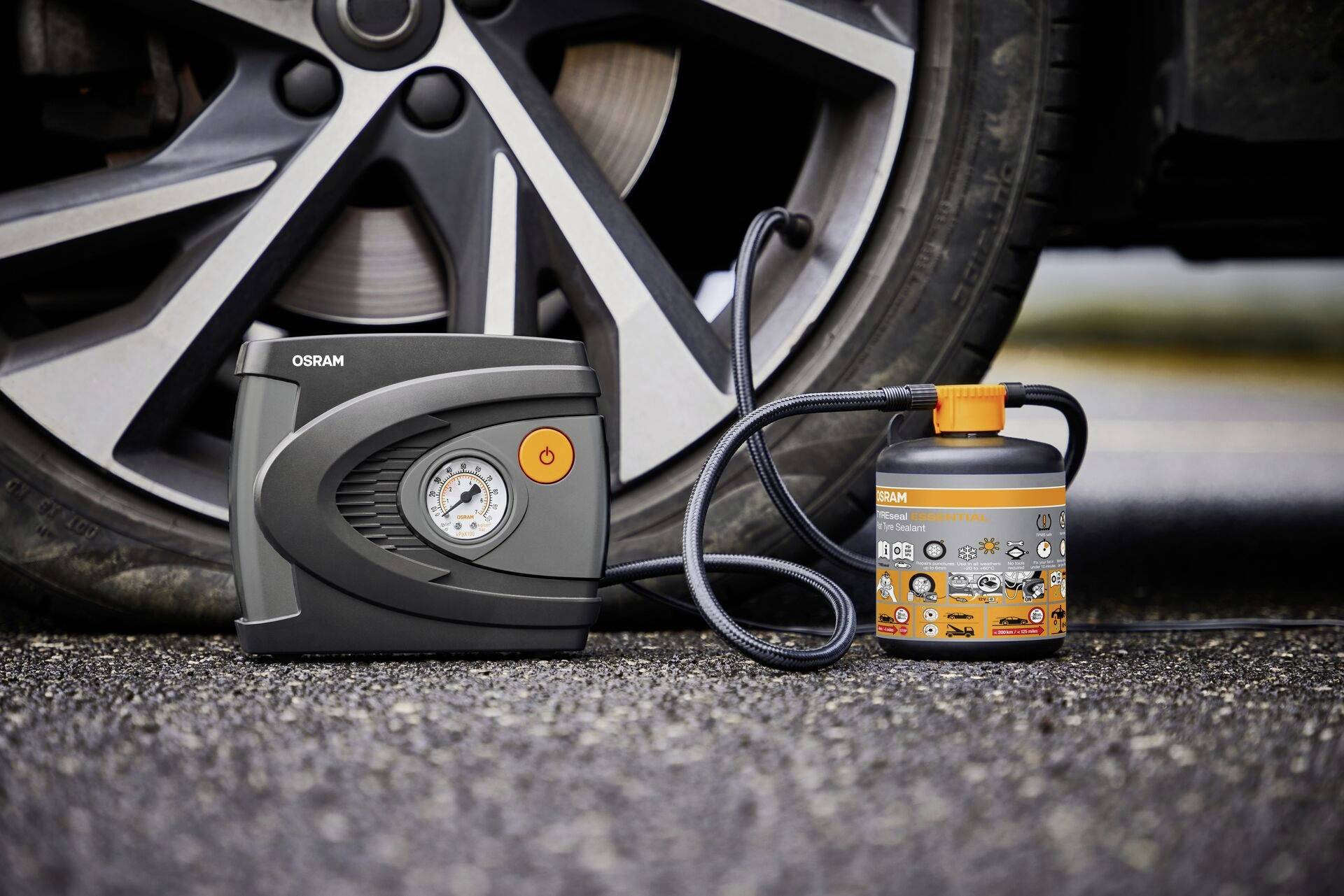 'Tyre inflation kit placed next to car tyres; includes pressure gauge, connected with tube and liquid bottle.'