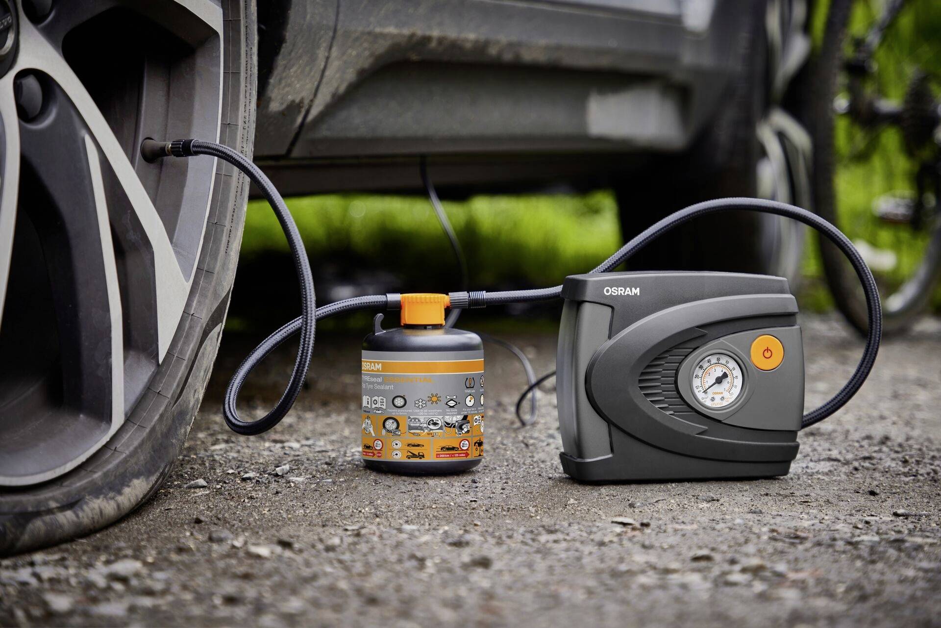 'Puncture repair kit next to car tyres, comprising an air compressor with pressure gauge and sealant container, ready for use.'