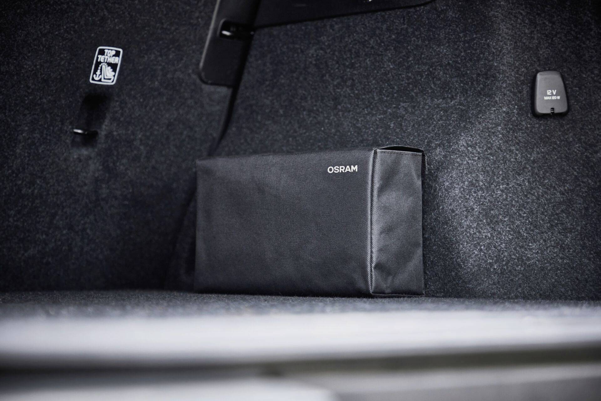 Black bag with 'OSRAM' inscription in a boot; carpet flooring and safety sticker visible.