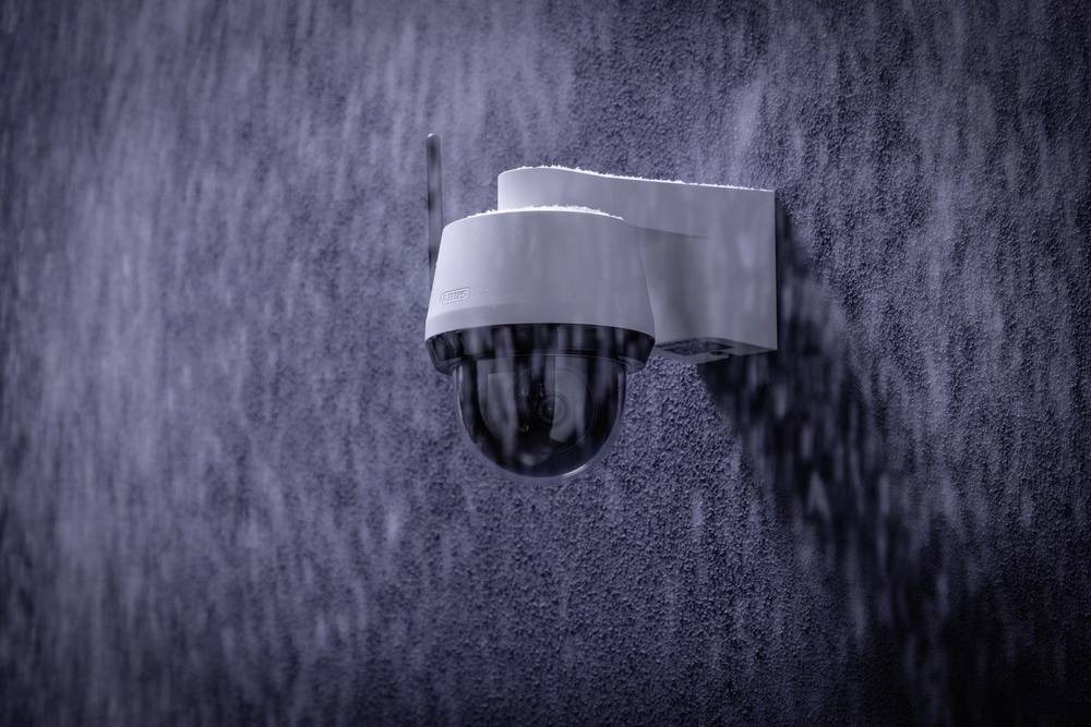 Security camera mounted on a wall in the rain.