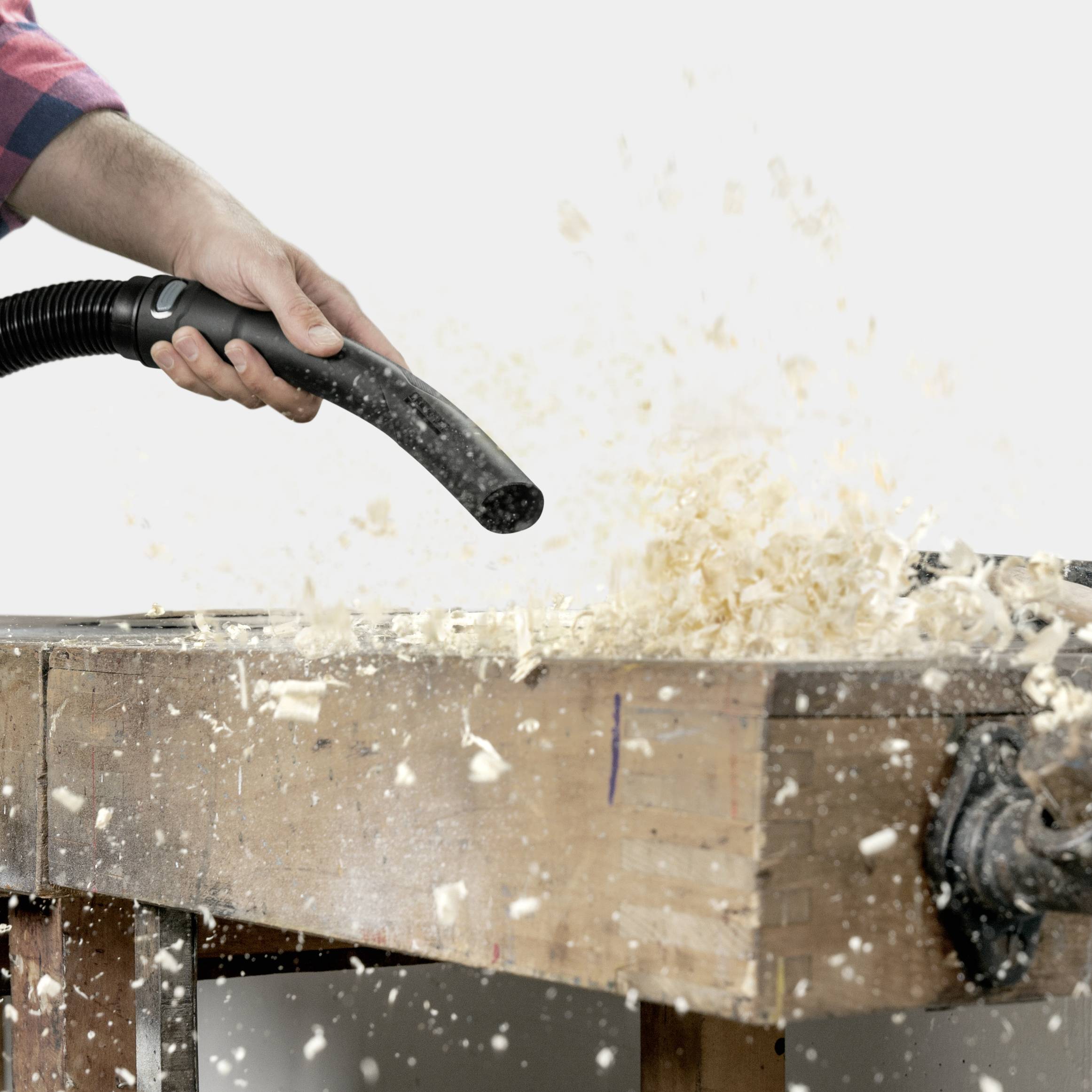 A person is vacuuming wood shavings from a workbench, indicating woodworking or carpentry.