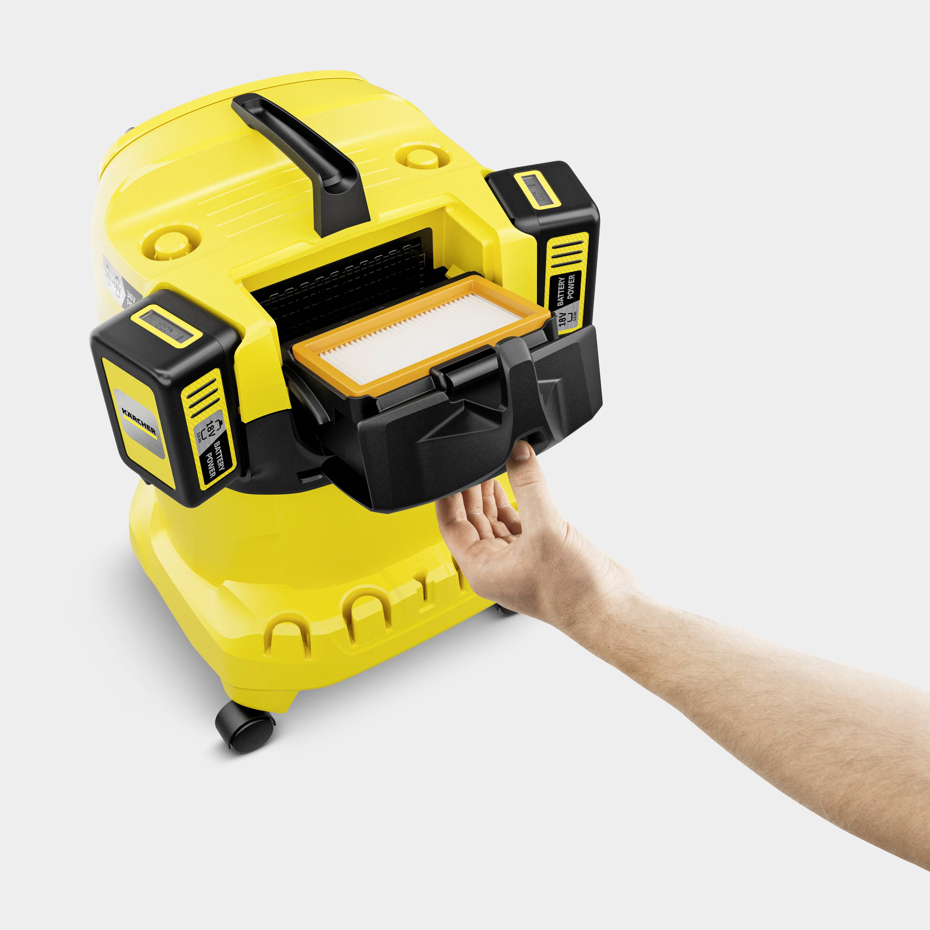 A hand removes a filter from a yellow vacuum cleaner. The vacuum cleaner is standing against a light background.