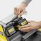 A hand is inserting a battery into a yellow battery charger. Another hand is holding the lid. The device and batteries are black and yellow.