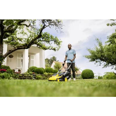 A man is mowing the lawn with a yellow lawnmower in the garden in front of a house. It is a sunny day with a green surrounding.