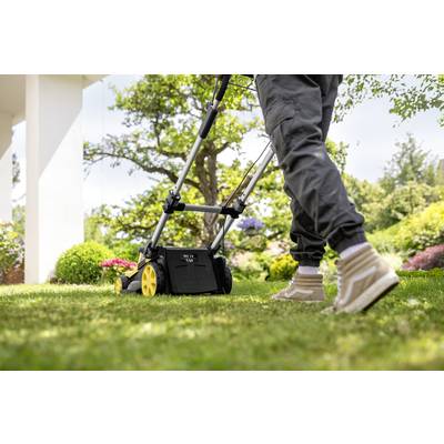 A person is mowing the lawn with a lawnmower in the garden. The focus is on the person's feet and the device.
