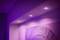 Lilac ceiling lighting illuminates a wall with an abstract artwork. The scene appears modern and atmospheric.