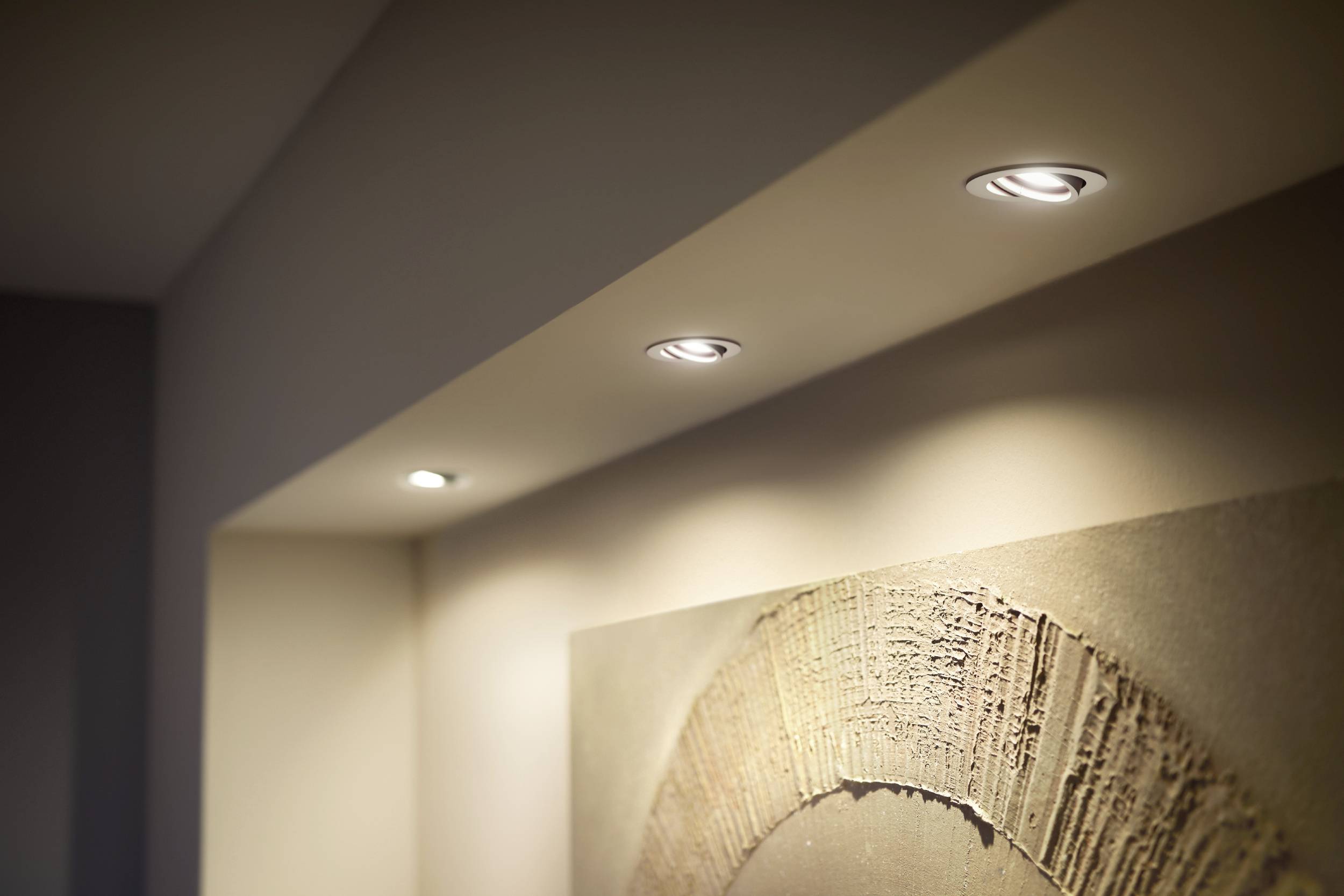 Ceiling spotlights illuminate the room with warm light. Beneath them, an artwork with structured, curved lines hangs on the wall.