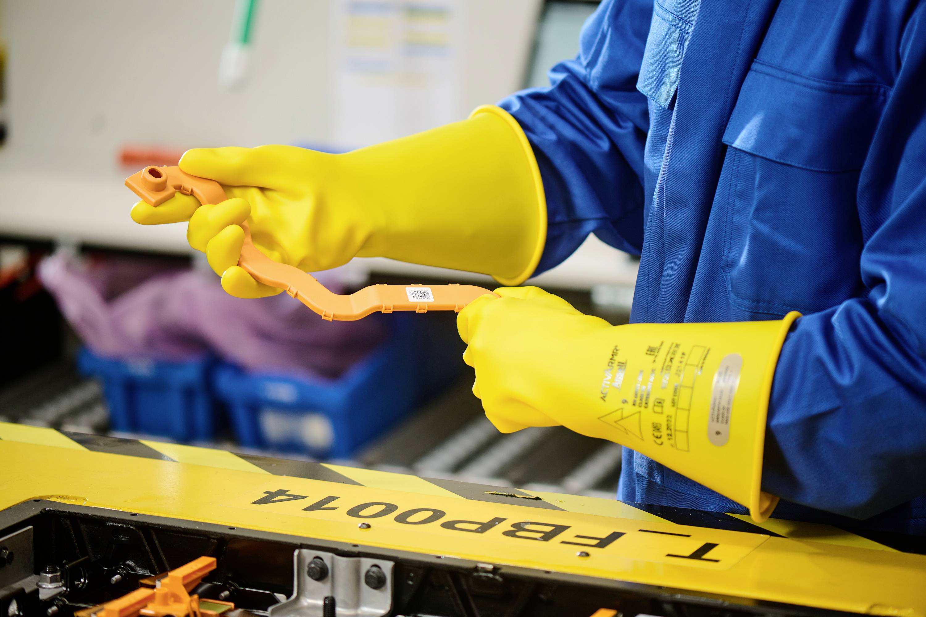 A person is wearing yellow protective gloves and working with components in a workshop environment, possibly on a technical device.