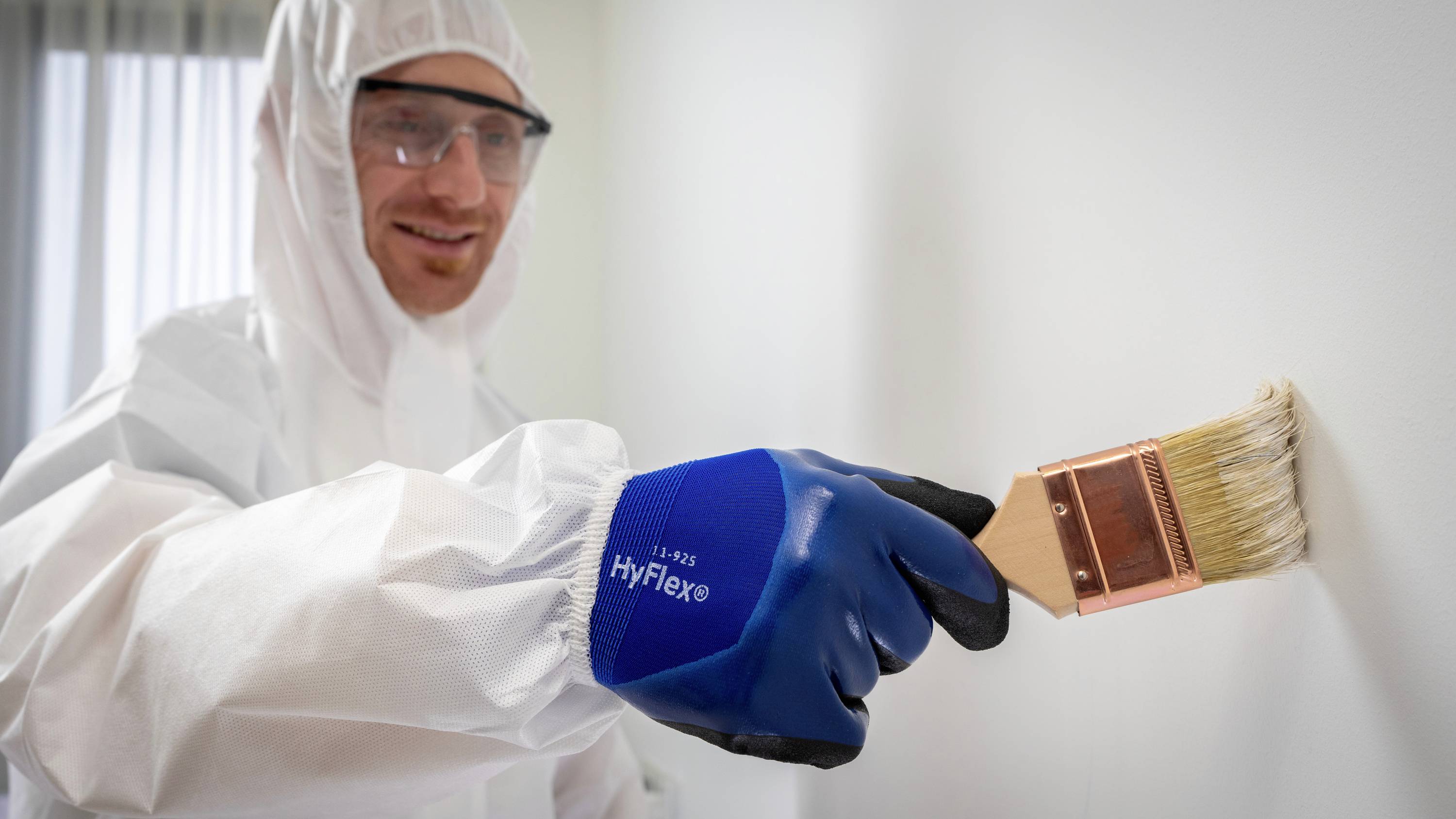 A person in protective clothing is painting a wall with a brush.